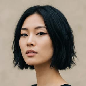 Portrait of East Asian woman with short black bob-cut hair with soft texture, sharp winged eyeliner, delicate facial structure, slightly parted natural lips, focused expression